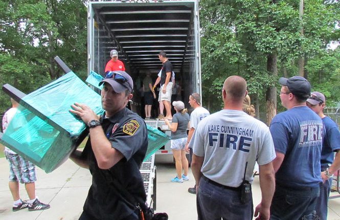 Firefighters and volunteers unloading furniture from a truck for an injured soldier