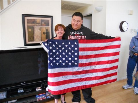 Beth Phillips and Staff Sergeant Oscar Canon holding an American flag in his furnished home